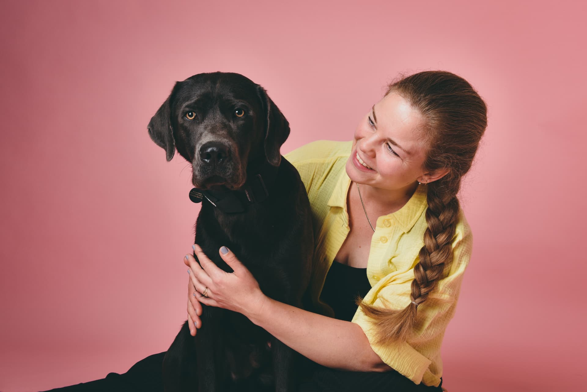 Karina sitzt eng an ihren Hund Rumi geschmiegt vor rosa Studiohintergrund